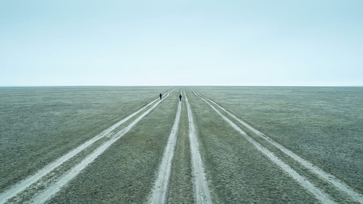 Tre piste parallele in pianura che convergono all'orizzonte, con due figure lontane