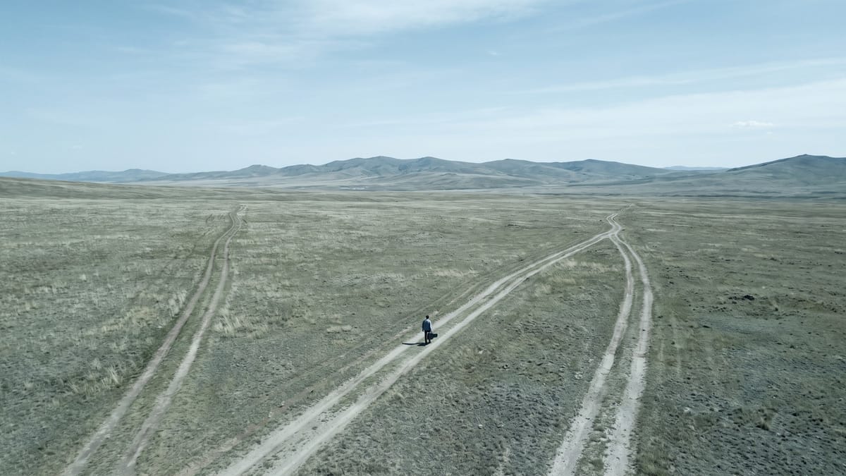 Altopiano con tre sentieri che si separano e una figura lontana che ne percorre uno